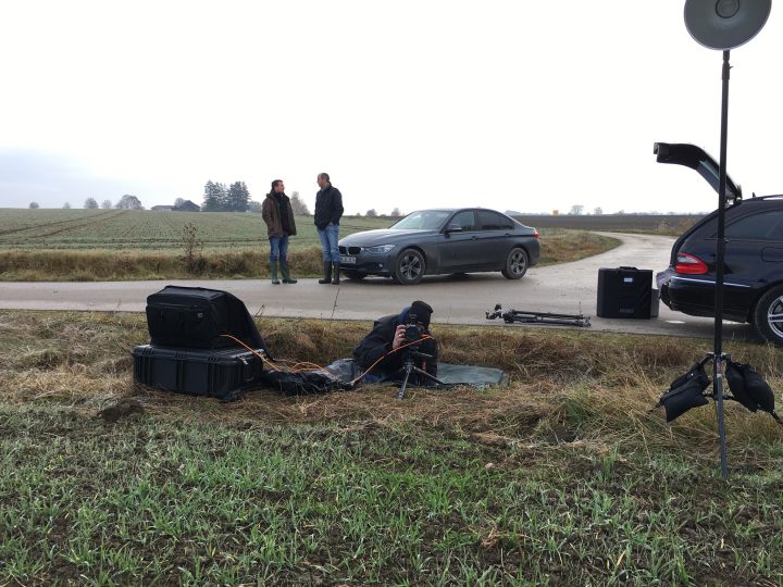 Fotograf fotografiert auf Landstraße, zwei Männer im Hintergrund.