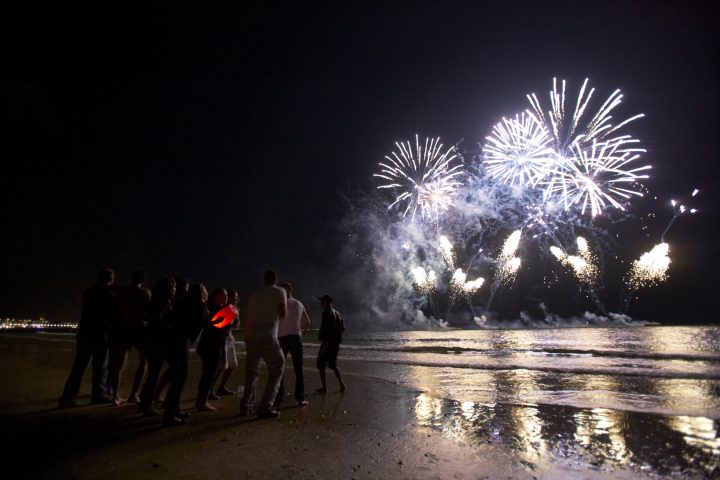 Gruppe beobachtet Feuerwerk am Strand bei Nacht.