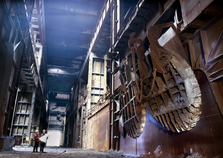 Industrielle Werkshalle mit zwei Ingenieuren, Kräne im Hintergrund.