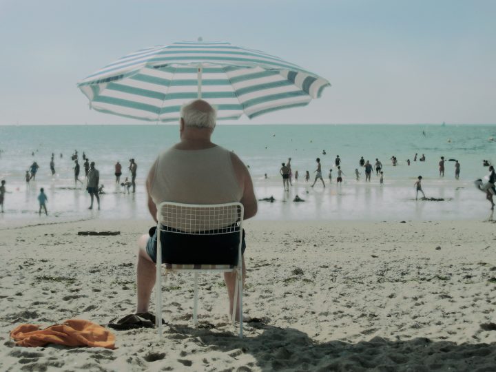 Mann am Strand unter gestreiftem Sonnenschirm