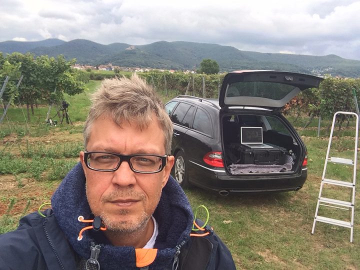 Mann auf Weinberg mit Auto und Laptop
