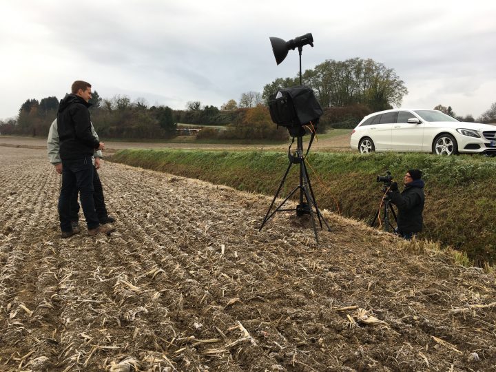 Outdoor-Fotoshooting auf einem Feld mit Auto im Hintergrund.