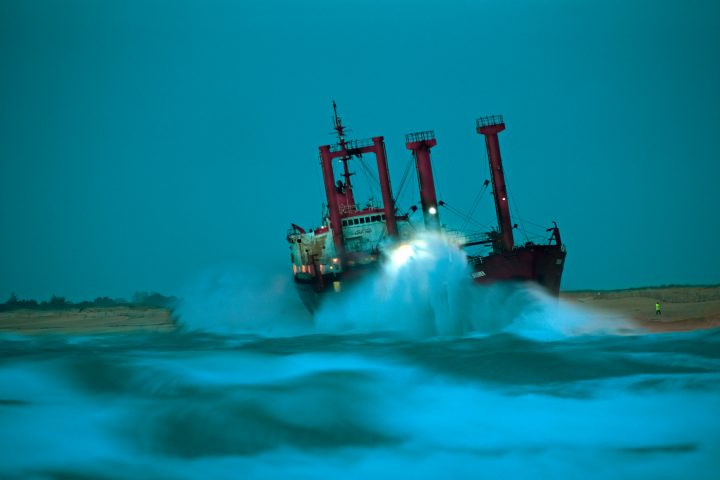Rotes Schiff im stürmischen Meer, nahe Sandküste
