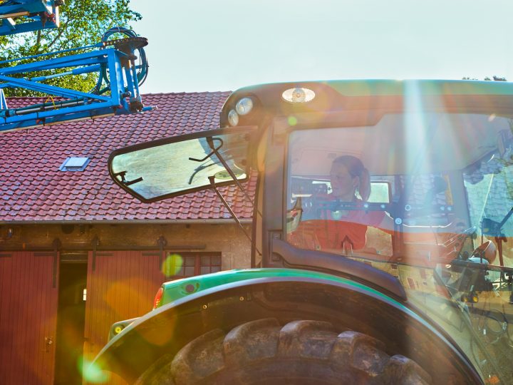 Frau fährt Traktor vor Scheune im Sonnenlicht.