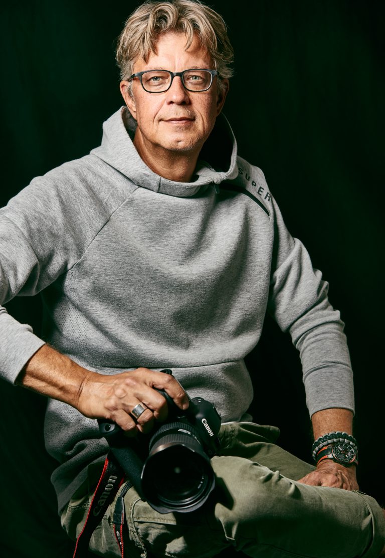 Mann mit grauem Pullover hält Kamera
