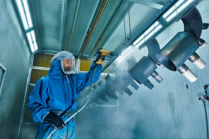 Arbeiter im Schutzanzug sprüht Metallteile in Werkstatt