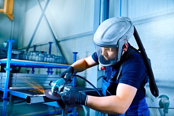 Arbeiter schleift Metall mit Schutzhelm und Schleifmaschine.