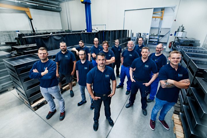 Team in Fabrikhalle mit Metallteilen