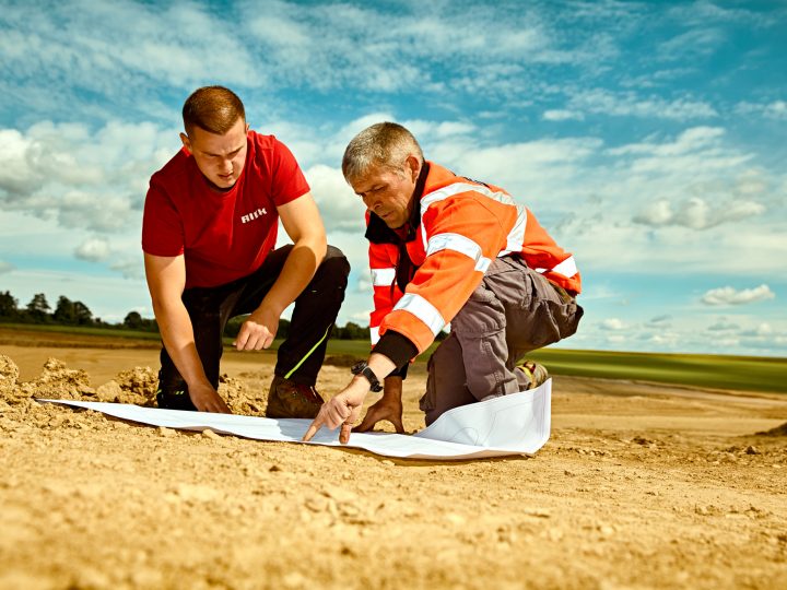 Arbeiter prüfen Baupläne auf Baustelle im Freien.