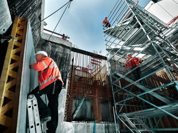 Bauarbeiter auf Baustelle mit Gerüst und Wänden.
