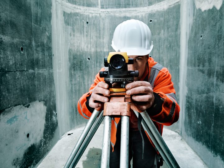 Bauarbeiter mit Nivelliergerät im Einsatz auf Baustelle.