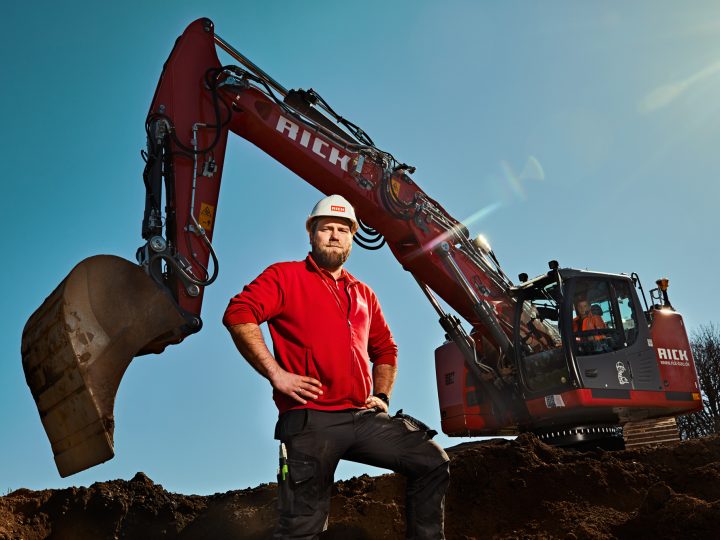 Bauarbeiter neben großem roten Bagger auf Baustelle