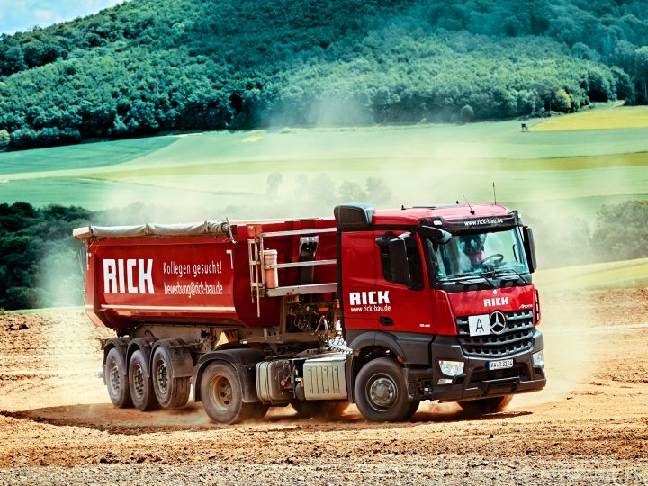 Roter Lastwagen fährt auf staubiger Straße.