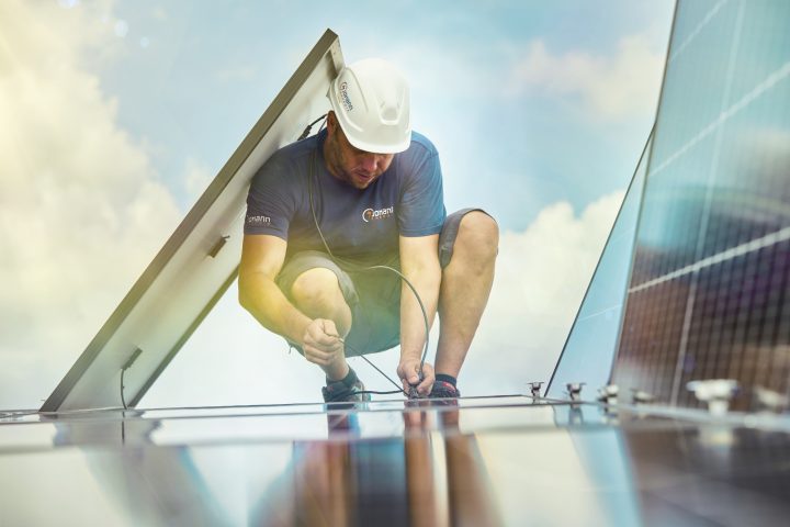 Arbeiter installiert Solarmodul auf Dachfläche, sonniger Tag