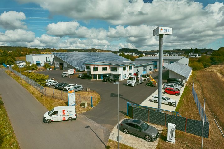 Industriegebäude mit Solarpanels und Fahrzeugen im Hof.